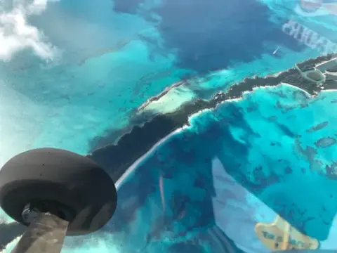 View from a small airplane over turquoise shallow water and sandbars, with the wheel and strut in the foreground