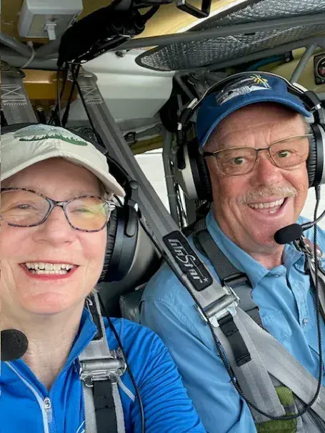 Two pilots in headsets smiling in the cockpit of a small airplane