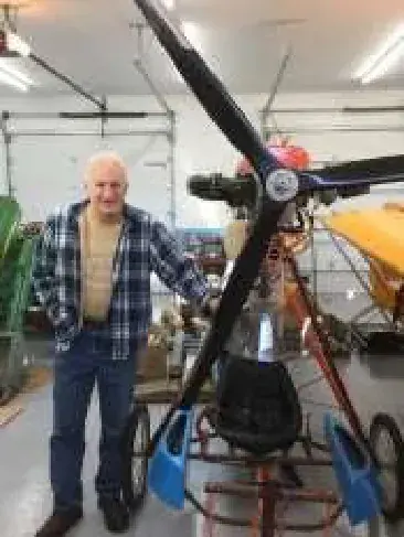 An older man standing beside an airplane propeller