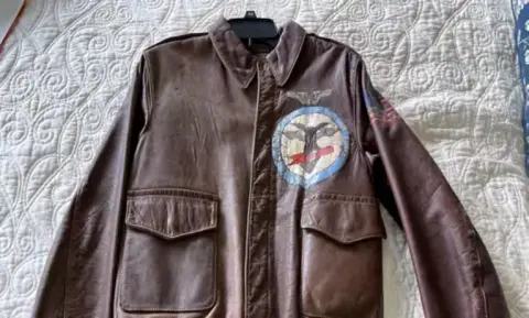 Brown leather flight jacket with a squadron patch, laid flat