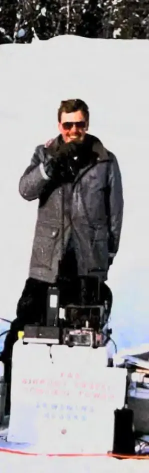 Person in a long coat standing in deep snow beside a pole
