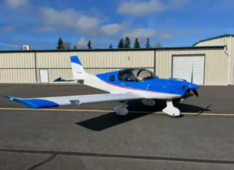 A blue and white low-wing airplane on the ramp in front of a hangar
