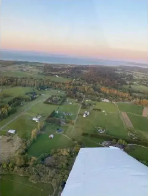 Farmland and houses seen from the air below a wing at dusk