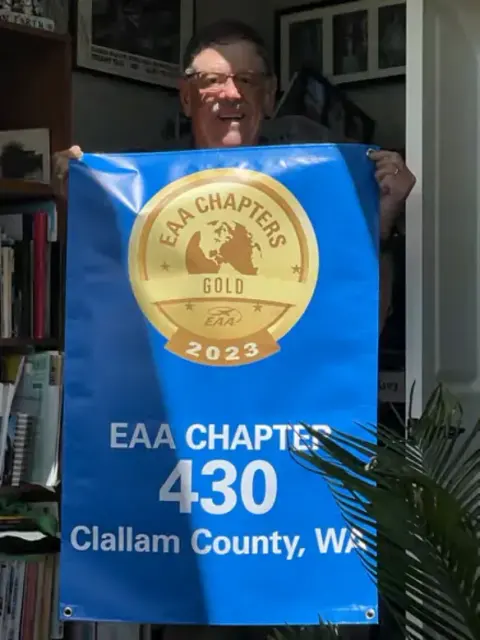 Person holding up a blue EAA Chapter 430 Clallam County banner