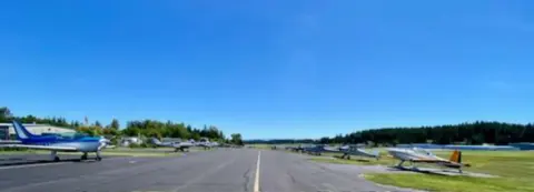 Grass and paved airstrip with parked airplanes under a blue sky