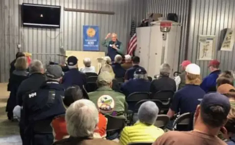 Audience seated in a hangar for a presentation
