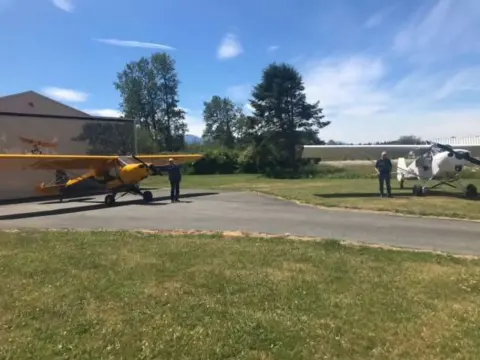 Two Cubs on a grass strip beside a hangar