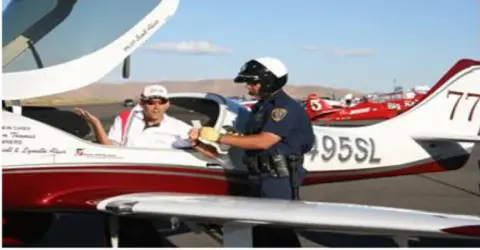 Race official talking with the pilot of a red and white airplane numbered 77