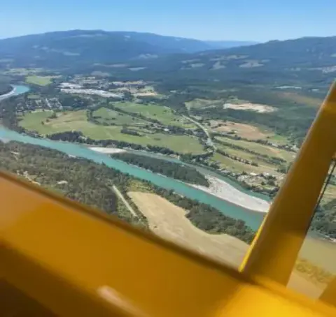 View past the yellow wing strut of a Cub over a river valley and farmland