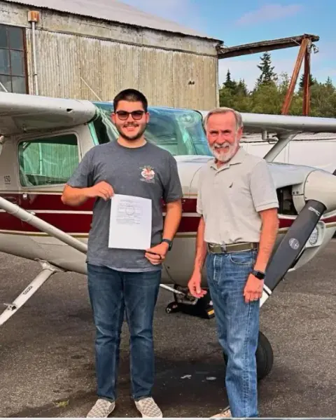 New pilot holding a certificate beside his instructor and a training airplane