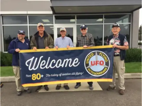 Group holding a Welcome United Flying Octogenarians banner