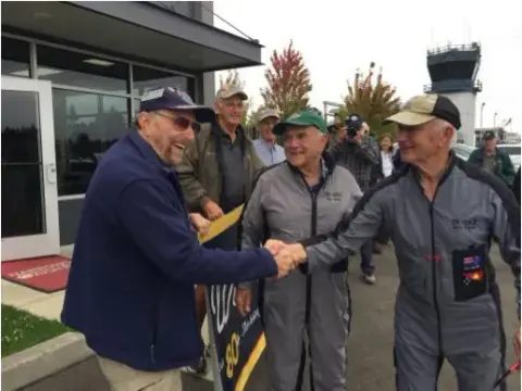 Men in flight suits greeting a visitor outside a terminal