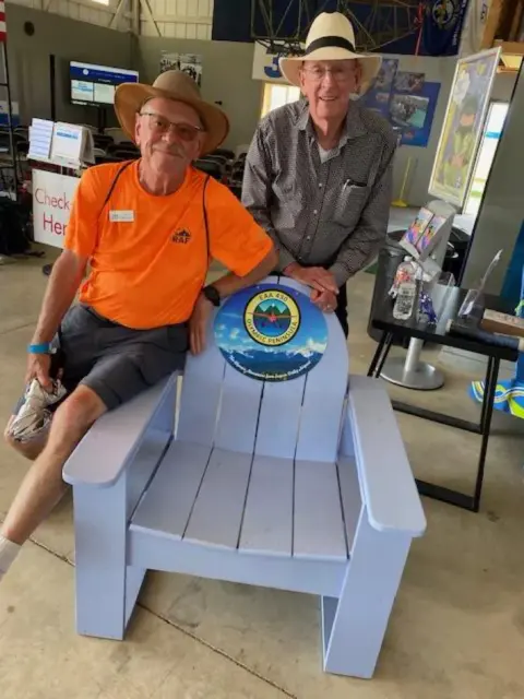 Man in an orange shirt sitting in a white Adirondack chair in front of the EAA chapter map