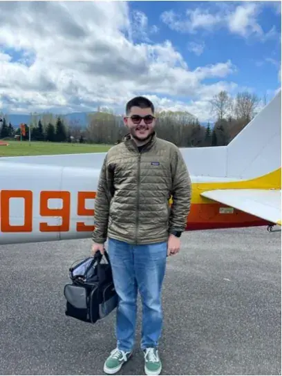 Young pilot holding a flight bag beside an airplane
