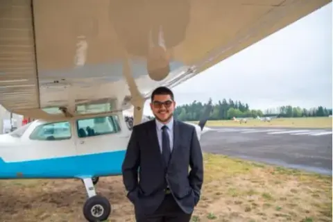 Young man in a suit standing under the wing of a Cessna