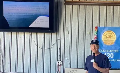 Man speaking in front of a hangar with an EAA Chapter 430 banner