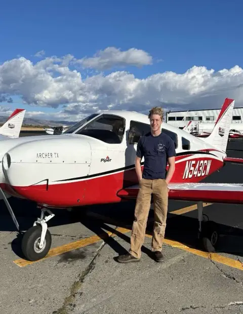 Young man standing beside the nose of a red and white low-wing airplane