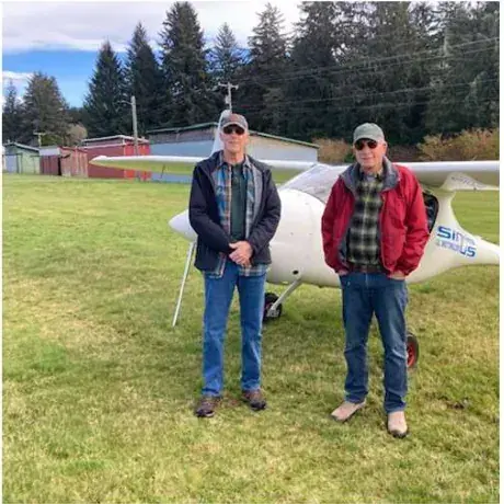 Two men standing on the grass in front of a parked airplane