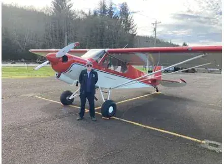 Pilot standing beside a red and white high-wing airplane