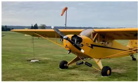 Yellow J-3 Cub on the grass with a windsock behind