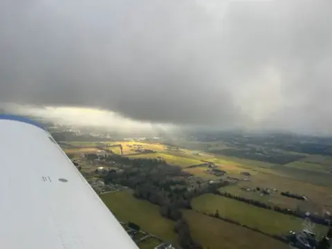 Wing of a small airplane over farmland under dark clouds