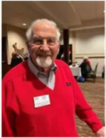 Older man in a red sweater with a name tag at an indoor gathering