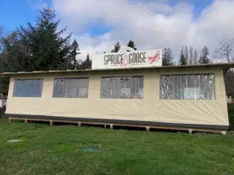 Restaurant building with a sign on the roof, seen across a lawn
