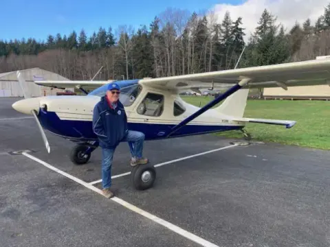 Pilot walking away from a blue and white low-wing airplane on a ramp