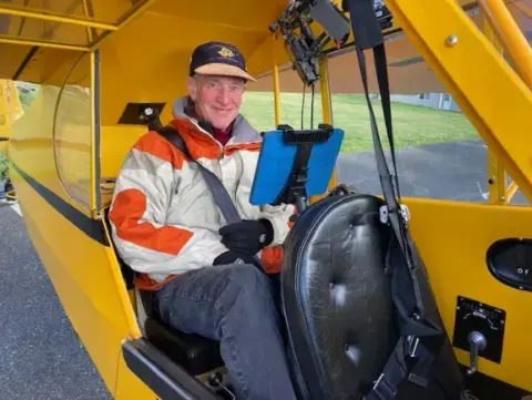 Smiling pilot in a headset sitting in the cockpit of a yellow airplane