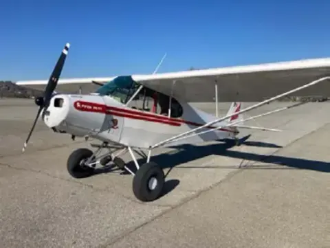 White and red Piper Cub-type airplane parked on a ramp