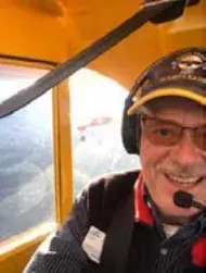 A smiling pilot in a headset and cap in the cockpit of a yellow airplane