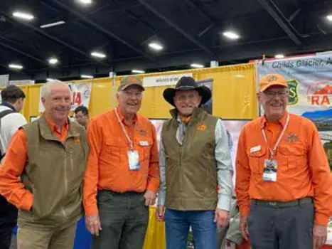 Four men in orange and green shirts at a trade show booth