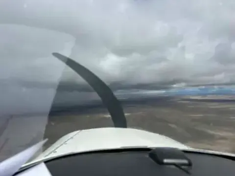 View over the nose of a small airplane flying under gray clouds