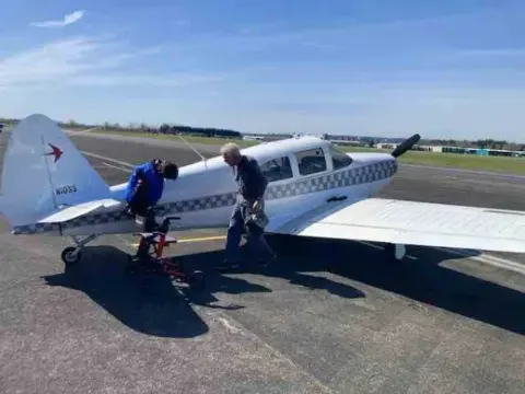 Silver low-wing airplane with a blue stripe on the ramp