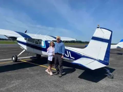Pilot and passenger beside a blue and white low-wing airplane with a T-tail