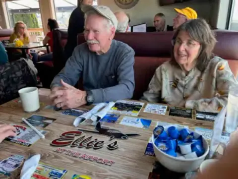 Man and woman at a restaurant table with model airplane parts