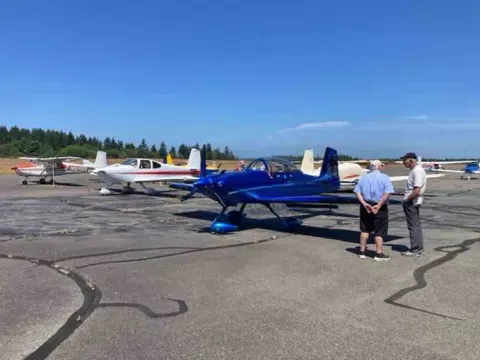 Pilots beside a blue and red low-wing airplane on the ramp
