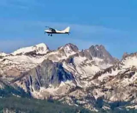 Small airplane flying over snow-covered mountain peaks