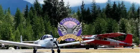 Two airplanes on the grass at the Concrete airport, a white low-wing and a red high-wing, with the Old Fashioned Concrete Fly-In logo