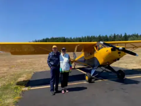 Two people standing beside a yellow Cub on a grass field