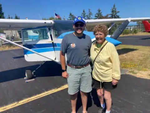 A man and a woman standing beside a parked high-wing airplane