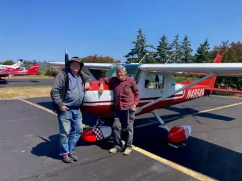 Two men standing beside a red and white high-wing airplane