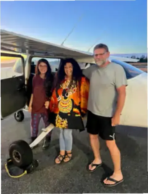 Three people standing together beside an airplane