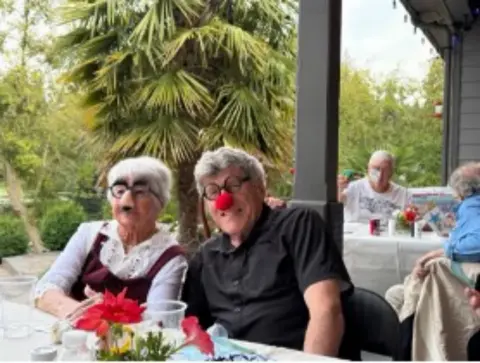 Couple at the board dinner table, one wearing a red clown nose