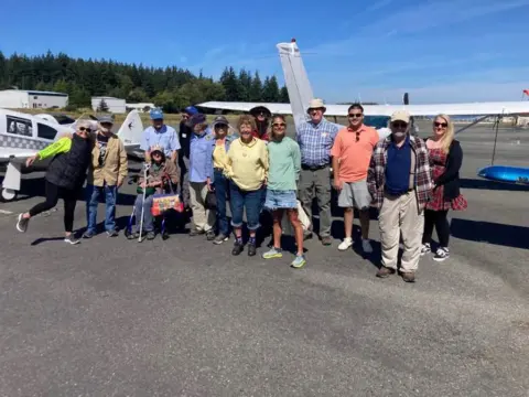 Group of fly-out participants posing in front of airplanes on Orcas Island