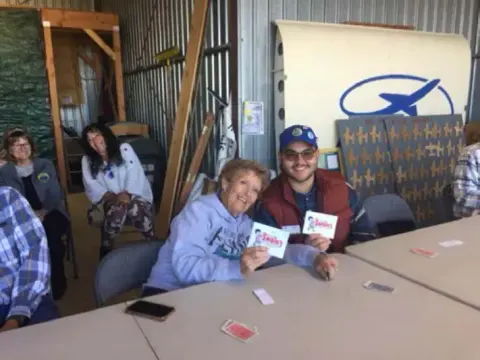 Two players holding up their cards at a table in the hangar