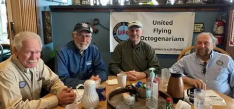 Group of older pilots having breakfast at a café table