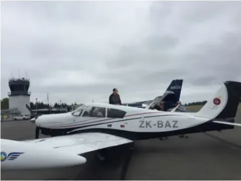 White low-wing airplane with registration ZK-BAZ on the ramp