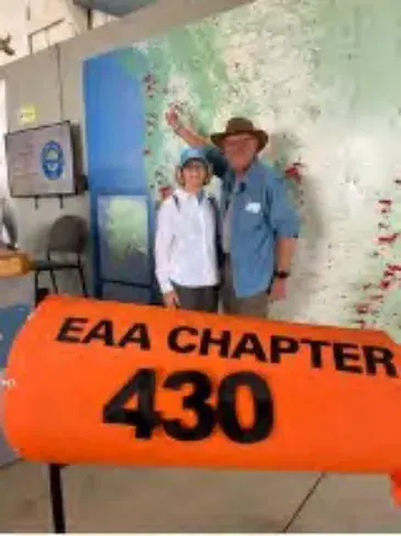 Two people beside an orange EAA Chapter 430 sign in front of a map