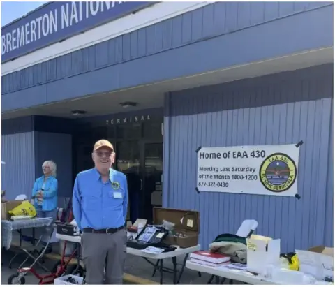 Member standing beside swap meet tables outside a hangar